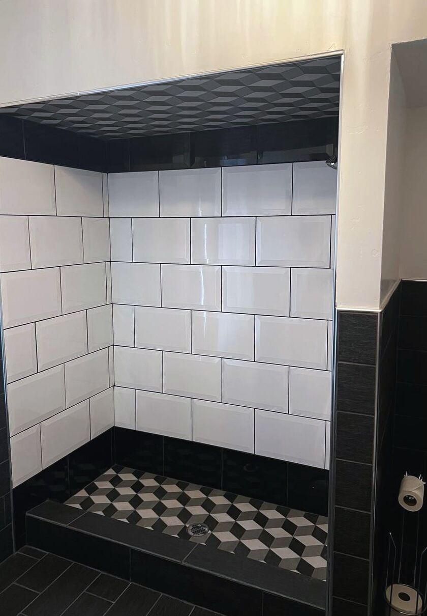 Fully tiled bathroom with a walk-in shower in white subway tile with a black geometric border