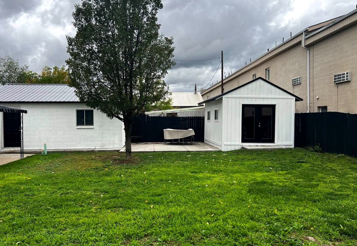 Back lawn with mature shade tree, concrete patio, block garage and a finished board-and-batten outbuilding
