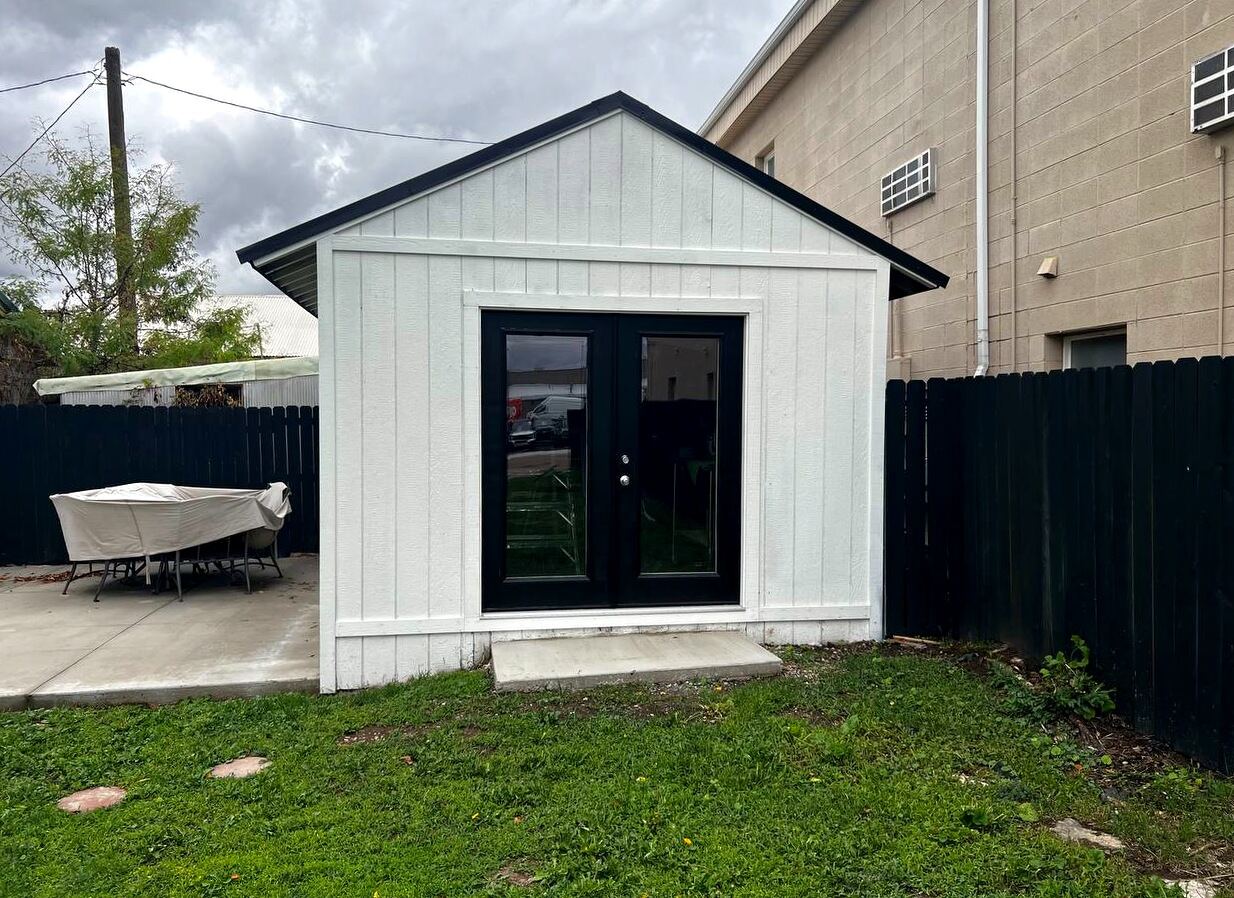 Finished board-and-batten outbuilding with black French doors, off the rear patio