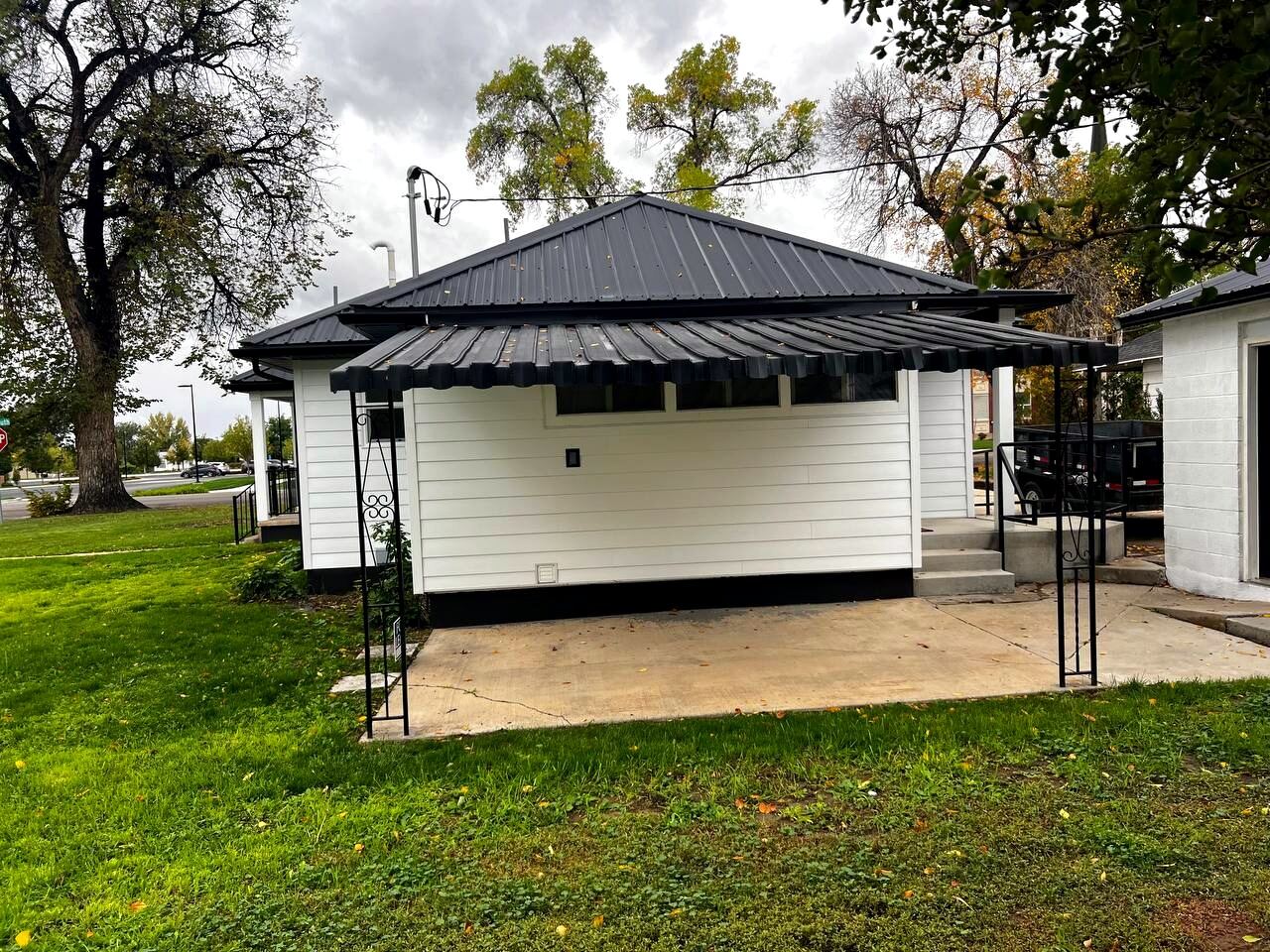 Wide view of the property — building, deep covered carport over a concrete parking pad, mature trees and corner-lot lawn